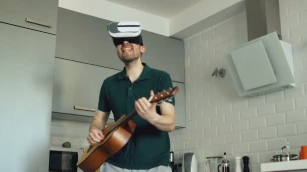 Jovem feliz dançando e tocando guitarra na cozinha usando o fone de ouvido VR 360 e sente-o guitarrista em concerto em casa — Vídeo de Stock