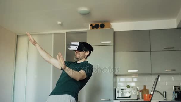 Забавный молодой человек в виртуальной реальности 360 гарнитура танцует на кухне утром, слушая музыку и весело провести время дома — стоковое видео