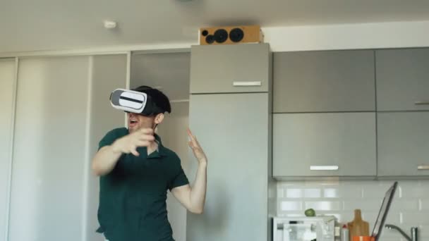 Srandovní mladý muž v soupravu pro virtuální realitu 360 tanec v kuchyni ráno při poslechu hudby a zábavy doma — Stock video