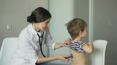 Küçük çocuk konuşmak ve dinlemek stetoskop tıbbi ofis ile genç bir kadın doktor