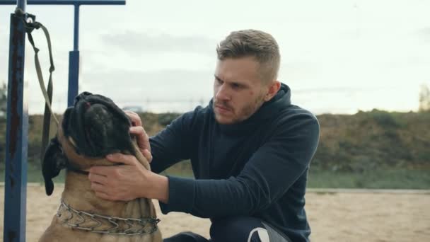 Joven hombre deportivo abrazo y jugar su bullmastiff perro al aire libre en la naturaleza — Vídeos de Stock