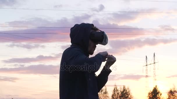 Slowmotion de silueta del joven boxeador en VR 360 entrenamiento de auriculares para patear en combate de realidad virtual al atardecer en el parque de la ciudad — Vídeo de stock