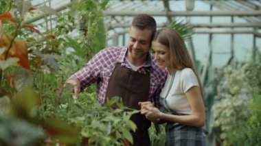 Mutlu genç çiçekçi kaç serada çalışan önlük içinde. Neşeli kadın kucaklama kocası Çiçek Bahçe pot ile sulama
