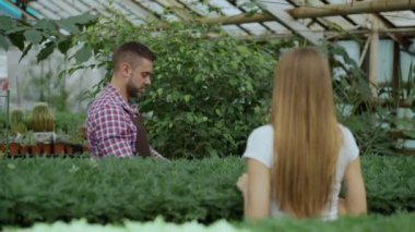 Genç gülümseyen satıcı çiçekçi Bahçe merkezinde çalışıyor. Kadın müşteri ve mağaza kredi kartı ile ödeme yapmadan alışveriş çantası sağlar