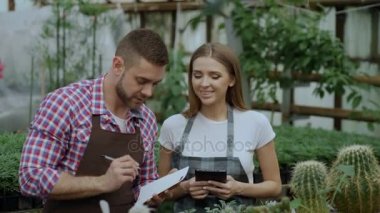 Genç Bahçe merkezinde çiçekçi iş çift. Çekici bir adam cheking çiçek ve serada çalışma sırasında tablet bilgisayar kullanan kadın