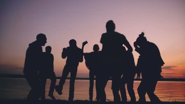 Silueta de grupo jóvenes bailando tienen una fiesta en la playa al atardecer — Vídeo de stock