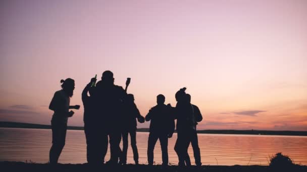 Silhouet van een groep jonge mensen dansen hebben een partij op strand op zonsondergang — Stockvideo
