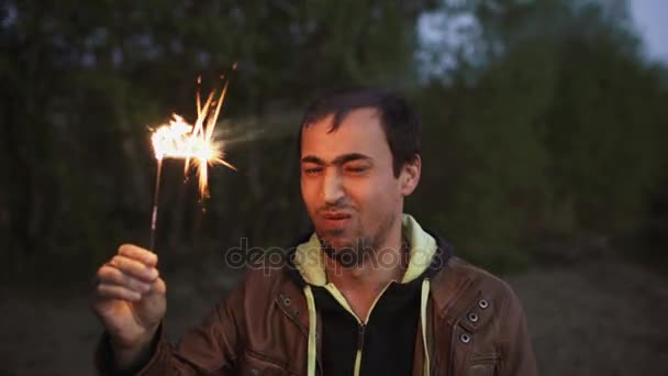Retrato de jovem sorridente homem com sparkler comemorando na festa na praia — Vídeo de Stock