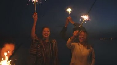 Grup genç arkadaşlar beach parti. Dans ve havai fişekleri ile alacakaranlık günbatımı kutlayan arkadaşlar