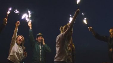 Ağır çekim genç arkadaşlar beach parti grubunun. Dans ve havai fişekleri ile alacakaranlık günbatımı kutlayan arkadaşlar