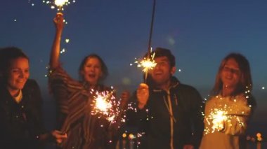 Genç arkadaşının plaj partisi Slowmotion grubu. Dans ve havai fişekleri ile alacakaranlık günbatımı kutlayan arkadaşlar