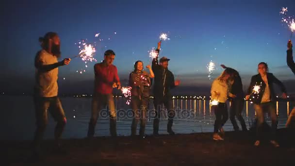 Un gruppo di giovani amici che danno una festa in spiaggia. Amici che ballano e festeggiano con scintille al tramonto — Video Stock