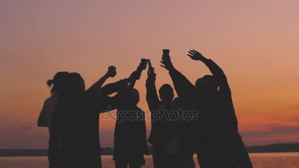 Movimento lento de grupo silhueta jovens dançando aplausos e dar uma festa na praia ao pôr do sol — Vídeo de Stock