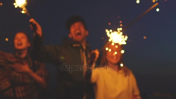 Slowmotion група молодих друзі пляжну вечірку. Друзі, танцювали і святкували з бенгальські вогні в сутінки захід сонця — стокове відео
