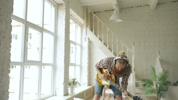 Grappige bebaarde man dans op bed zingt en speelt gitaar in slaapkamer thuis — Stockvideo