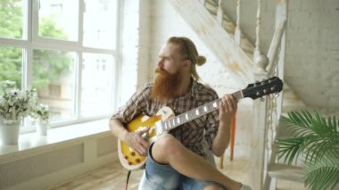 Modern yatak odası evde gitar çalmayı sandalye üzerinde oturan çekici sakallı adam