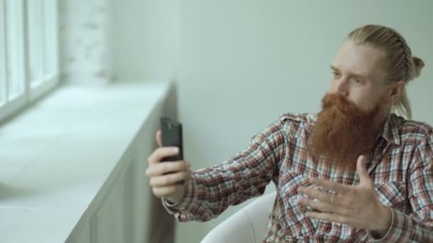 Skäggig ung hipster affärsman talar videochatt på smartphone medan du sitter i offce stol — Stockvideo