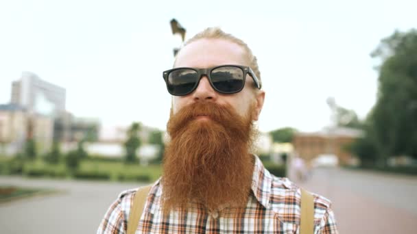 Πορτρέτο του hipster γενειοφόρο άτομο τουριστικά σε γυαλιά ηλίου βλέπουν φωτογραφική μηχανή και να χαμογελά σε φόντο πόλη — Αρχείο Βίντεο