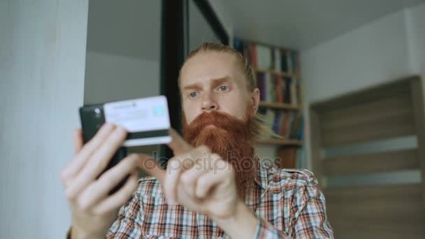 Бородатий чоловік онлайн покупки та банківська справа з кредитною карткою за допомогою смартфона вдома — стокове відео