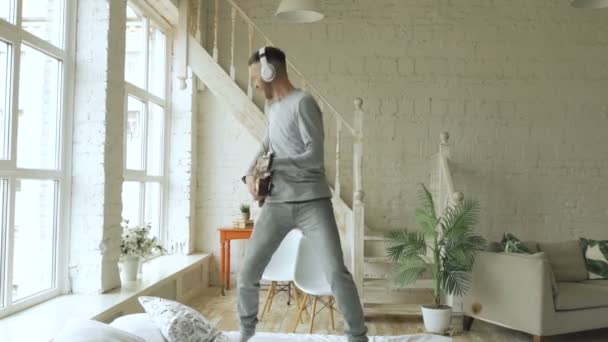 Slowmotion vicces szakállas férfi tánc ágyon, énekel és játszik az elektromos gitár a hálószobában otthon — Stock videók