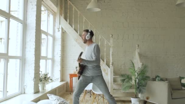 Забавный бородатый мужчина танцует на кровати, поет и играет на электрогитаре в спальне дома — стоковое видео
