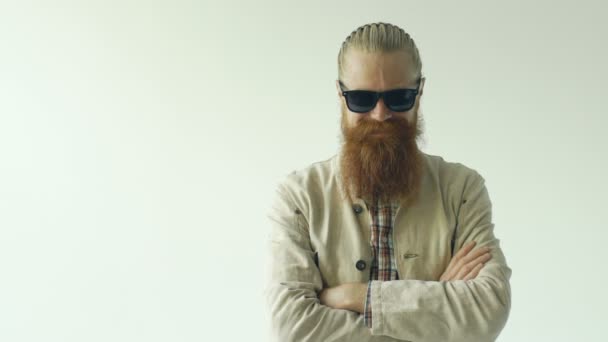 Retrato en cámara lenta del hombre hipster con gafas de sol mirando a la cámara y sonriendo sobre fondo blanco — Vídeos de Stock