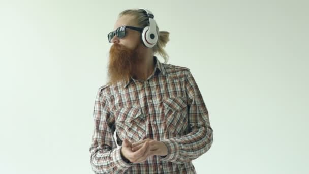 Slowmotion of Happy young bearded man in sunglasses and headphones dancing and listen music on white background — Stock Video