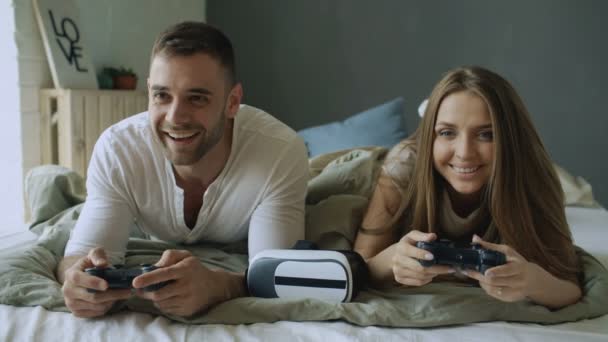 Young couple playing video copmuter games lying in bed at home — Stock Video