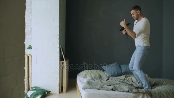 Jovem cantando ao secador de cabelo e dançando hiphop na cama no quarto — Vídeo de Stock