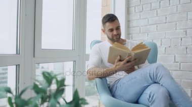 Genç adam modern daire balkonda oturup kitap okumak