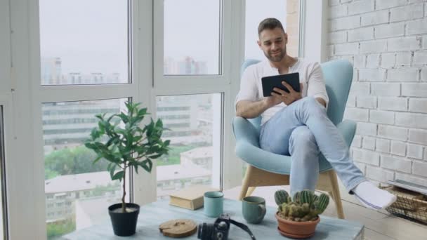 Ελκυστικά άνθρωπος χρησιμοποιώντας ψηφιακό tablet που κάθεται στην καρέκλα στο μπαλκόνι στο σύγχρονο διαμέρισμα σοφίτας — Αρχείο Βίντεο