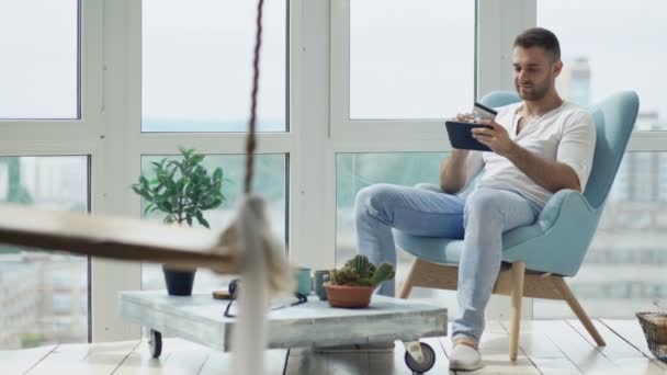 モダンな中二階のアパートのバルコニーに座ってデジタル タブレット コンピューターを使用してオンライン ショッピングを行う若い笑みを浮かべて男 — ストック動画