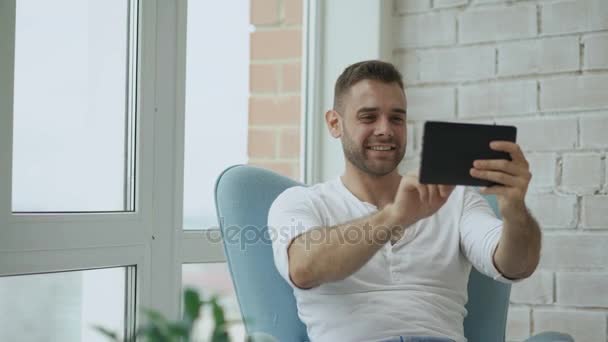 Jovem feliz homem tem chat de vídeo online usando tablet digital sentado na varanda no apartamento loft moderno — Vídeo de Stock