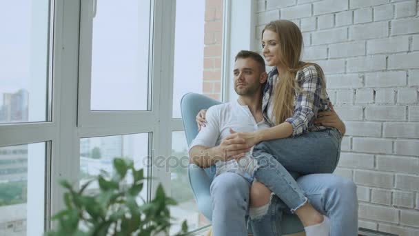 Hermosa pareja joven relajarse sentado en la silla y disfrutar de la vista desde el balcón del nuevo apartamento loft — Vídeos de Stock