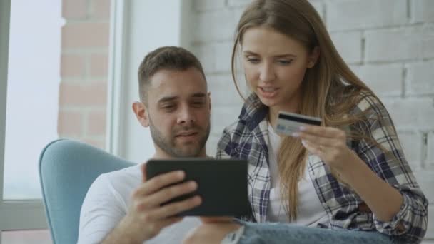 Νεαρό ζευγάρι χαρούμενα χρησιμοποιώντας ψηφιακή δισκίο υπολογιστή για online αγορές που κάθονται στο μπαλκόνι σε μοντέρνο διαμέρισμα — Αρχείο Βίντεο