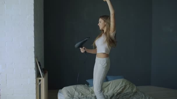 Młoda kobieta bawić, śpiewać z suszarka i taniec na łóżko w domu — Wideo stockowe
