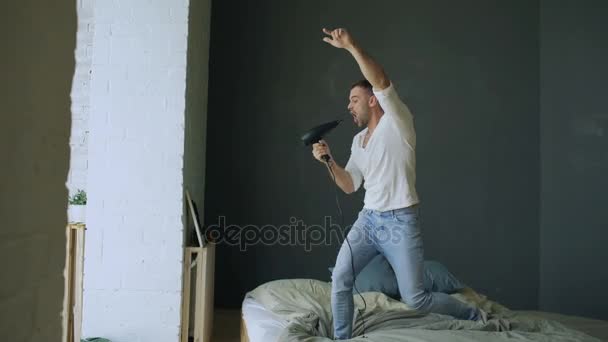 Młody mężczyzna śpiewu do włosów suszarką i taniec rocknroll na łóżko w sypialni — Wideo stockowe