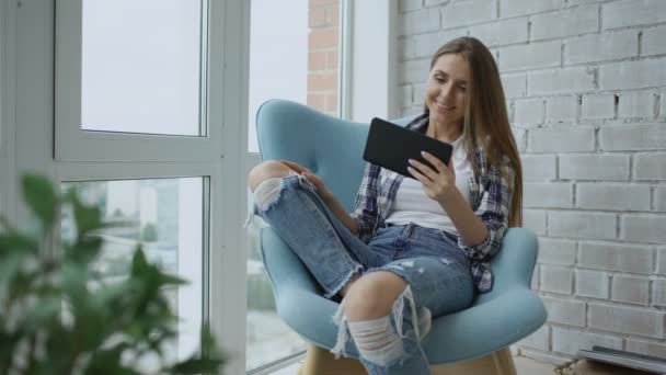 Jovem mulher sorridente tem bate-papo de vídeo online usando o computador tablet digital sentado na varanda no apartamento loft moderno — Vídeo de Stock