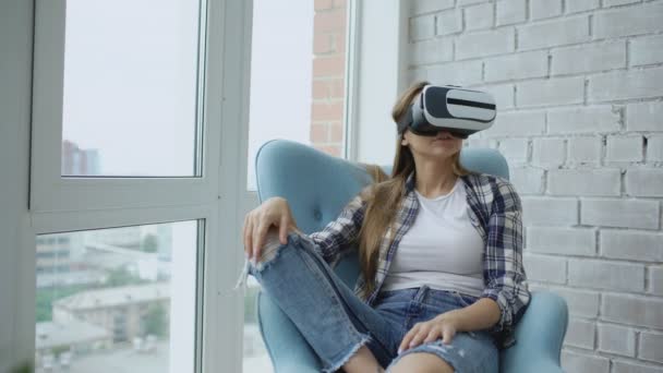 Jovem mulher tem experiência VR usando fone de ouvido realidade virtual sentado na cadeira na varanda — Vídeo de Stock