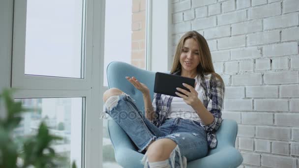 Молодая счастливая женщина имеют онлайн видео-чат, используя цифровой планшетный компьютер, сидя на балконе в современной квартире лофт — стоковое видео