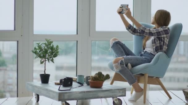 Молода щаслива жінка має онлайн-відео чат, використовуючи цифровий планшетний комп'ютер, що сидить на балконі в сучасній квартирі лофт — стокове відео