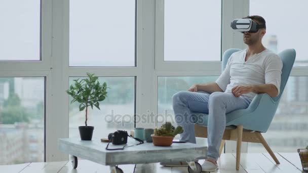 Jonge man zijn Vr ervaring met behulp van virtual reality headset voor het bekijken van de film zitten in de stoel op balkon — Stockvideo