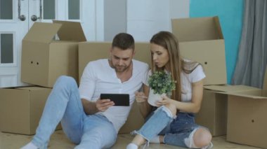 Genç çift yeni evlerinde taşındıktan sonra tablet bilgisayar kullanarak yerde oturuyor.