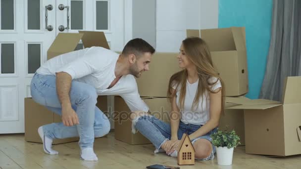 Happy couple sitting on floor in new house. Young man give keys to his girlfriend and kissing her — Stock Video