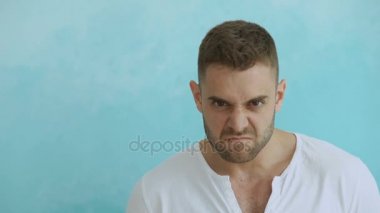 Kızgın genç adam kameraya mavi arka plan üzerinde seyir portresi