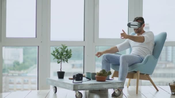 Młody człowiek ma Vr doświadczenie, aby grać w gry wyścigowe na komputerze przy użyciu zestaw wirtualnej rzeczywistości, siedząc w fotelu na balkonie — Wideo stockowe