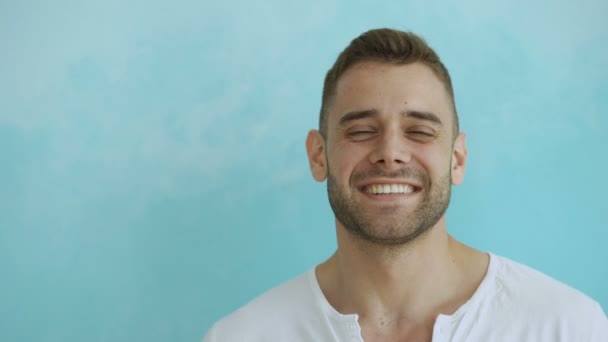 Portret zbliżenie ładny uśmiech i śmianie się człowiek patrząc w kamerę na niebieskim tle — Wideo stockowe
