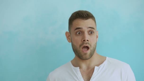 Porträt eines jungen Mannes, der aktiv überrascht und sich wundert, als er in die Kamera auf blauem Hintergrund blickt — Stockvideo