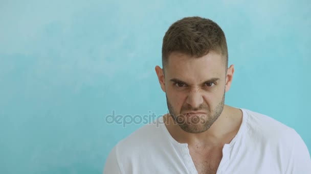 Retrato de un joven enojado mirando a la cámara sobre fondo azul — Vídeos de Stock