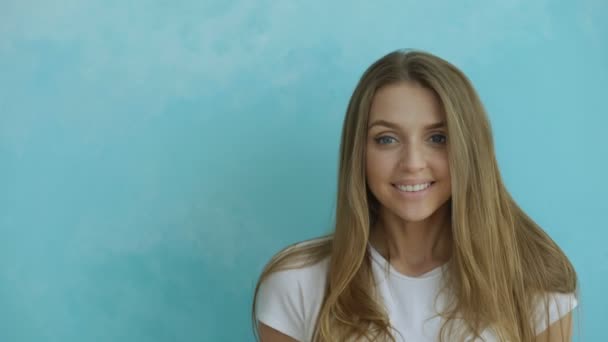 Closeup portret van jonge glimlachen en lachen vrouw op zoek naar camera op blauwe achtergrond — Stockvideo